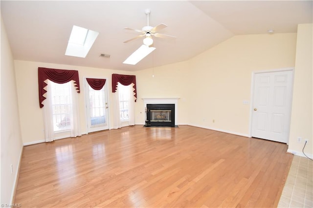 unfurnished living room featuring ceiling fan, vaulted ceiling with skylight, a fireplace with flush hearth, and light wood-style flooring