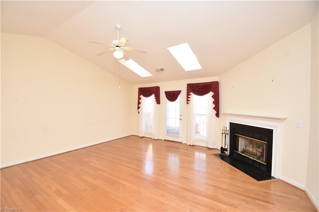 unfurnished living room with ceiling fan, a fireplace with flush hearth, baseboards, light wood finished floors, and lofted ceiling with skylight