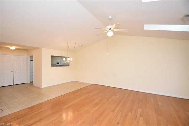 empty room featuring lofted ceiling, light wood-style flooring, baseboards, and ceiling fan with notable chandelier