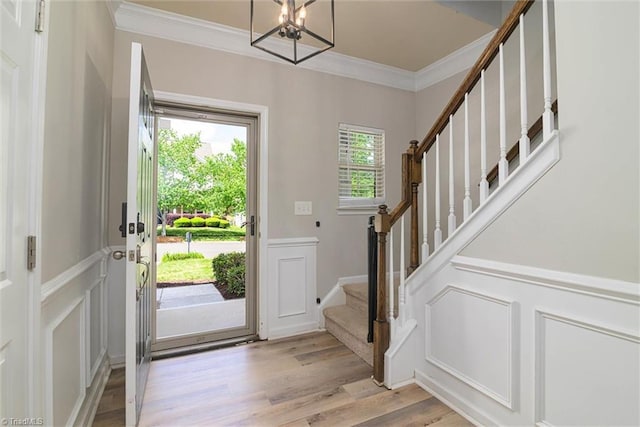 entrance foyer with crown molding, a notable chandelier, light wood-style floors, stairway, and a decorative wall