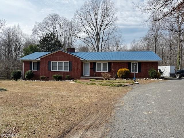 ranch-style home with driveway, a chimney, metal roof, and brick siding