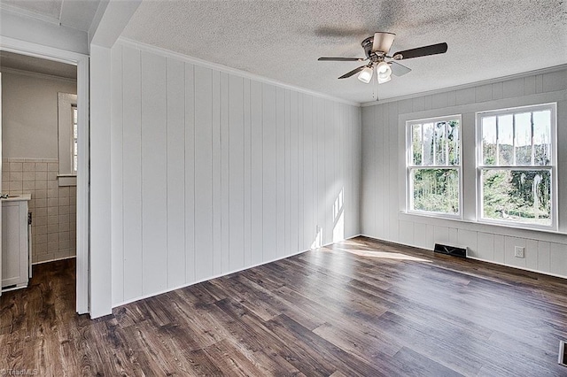 empty room with crown molding, visible vents, dark wood finished floors, and a textured ceiling