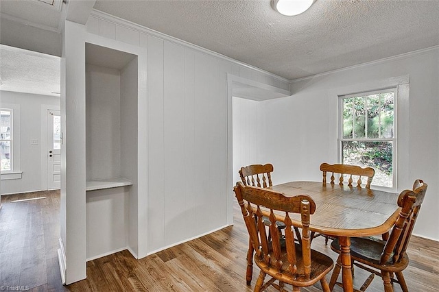 dining space featuring a textured ceiling, ornamental molding, and wood finished floors