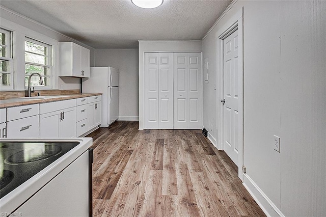 kitchen with white appliances, wood finished floors, a textured ceiling, white cabinetry, and a sink