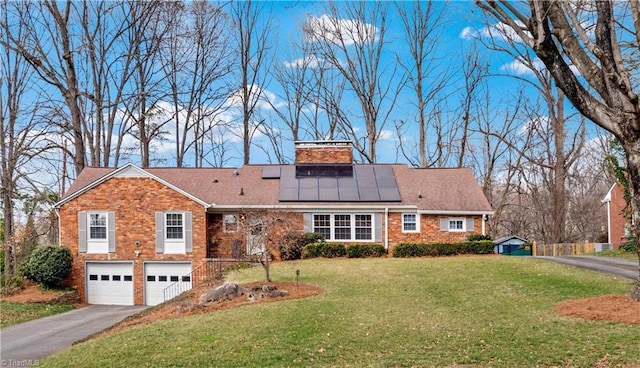 view of front of property featuring driveway, an attached garage, roof mounted solar panels, a front lawn, and brick siding