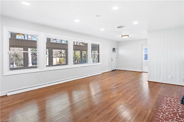 interior space featuring a baseboard radiator, baseboards, wood-type flooring, and a wealth of natural light