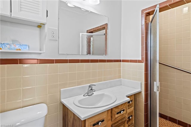 bathroom with toilet, vanity, tile walls, wainscoting, and a shower stall