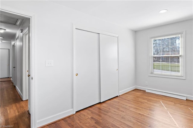 unfurnished bedroom featuring a closet, baseboards, baseboard heating, and wood finished floors