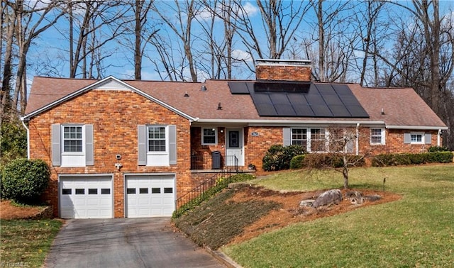 view of front of home with aphalt driveway, a garage, brick siding, roof mounted solar panels, and a front lawn