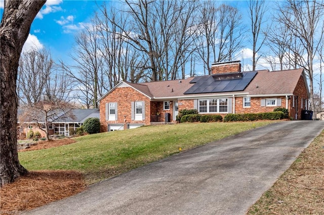 view of front of house featuring brick siding, a chimney, solar panels, an attached garage, and a front yard