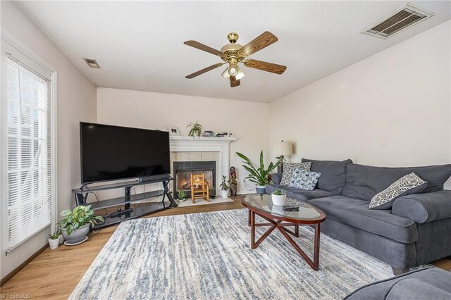 living room with ceiling fan, hardwood / wood-style flooring, and a tiled fireplace