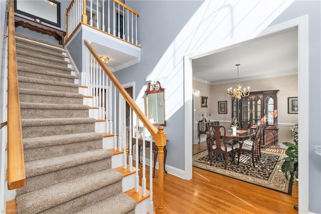 staircase with crown molding, wood-type flooring, an inviting chandelier, and a high ceiling