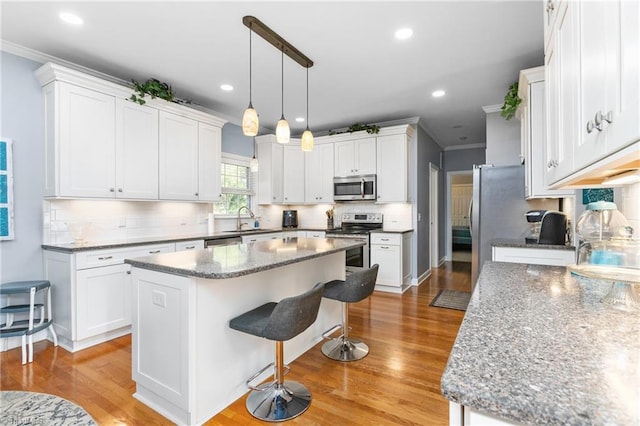 kitchen with a kitchen island, stainless steel appliances, crown molding, light wood-type flooring, and white cabinets