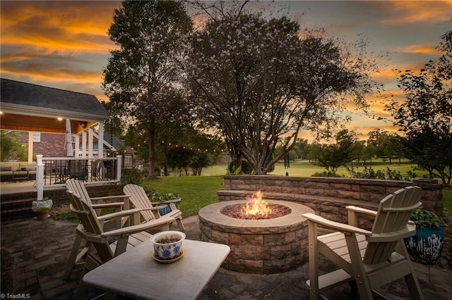 patio terrace at dusk featuring a wooden deck, a lawn, and a fire pit