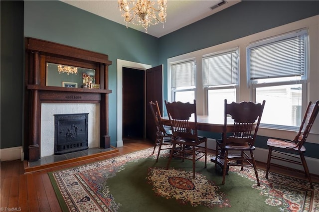 dining area with a fireplace, hardwood / wood-style floors, visible vents, baseboards, and a chandelier
