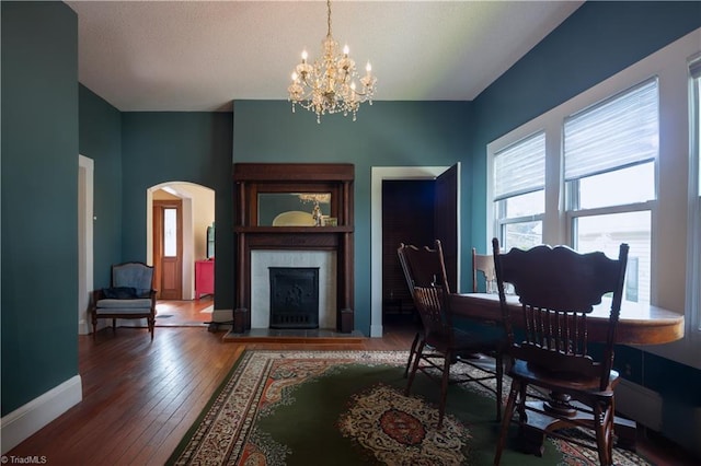 dining room featuring wood-type flooring, a fireplace, a notable chandelier, baseboards, and arched walkways
