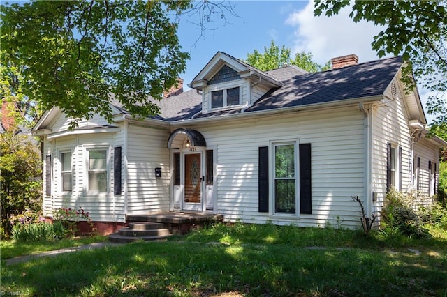 view of front of home with roof with shingles, a chimney, and a front yard
