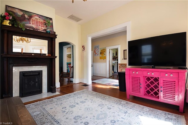 living area featuring wood finished floors, visible vents, wainscoting, arched walkways, and a high end fireplace