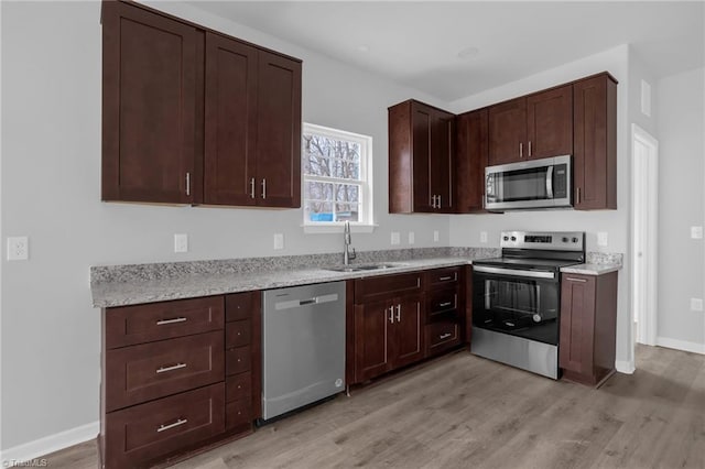 kitchen featuring dark brown cabinetry, appliances with stainless steel finishes, sink, light stone counters, and light hardwood / wood-style flooring