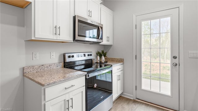 kitchen featuring white cabinetry, stainless steel appliances, light stone countertops, and light wood-type flooring