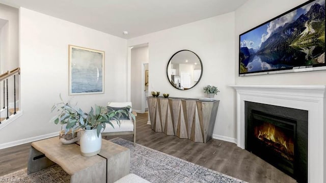 living room featuring stairs, wood finished floors, baseboards, and a warm lit fireplace