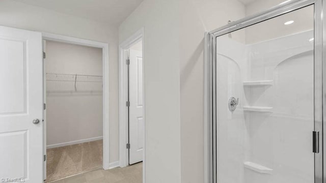 bathroom with a spacious closet, baseboards, and a stall shower