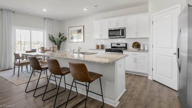 kitchen featuring dark wood-style floors, a center island with sink, appliances with stainless steel finishes, and a sink