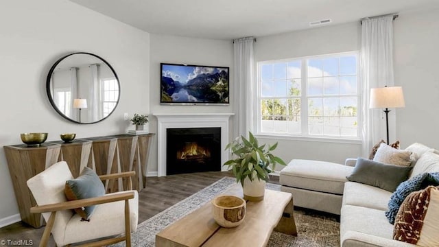 living room with baseboards, wood finished floors, visible vents, and a lit fireplace