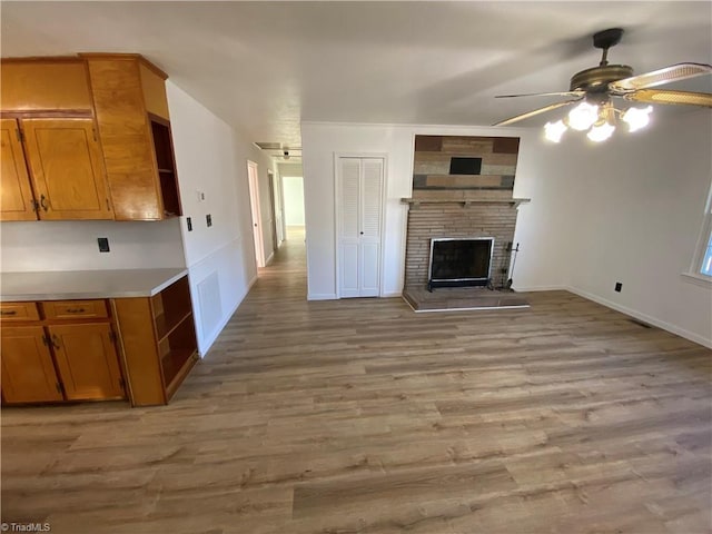 unfurnished living room featuring a brick fireplace, ceiling fan, and light wood-type flooring