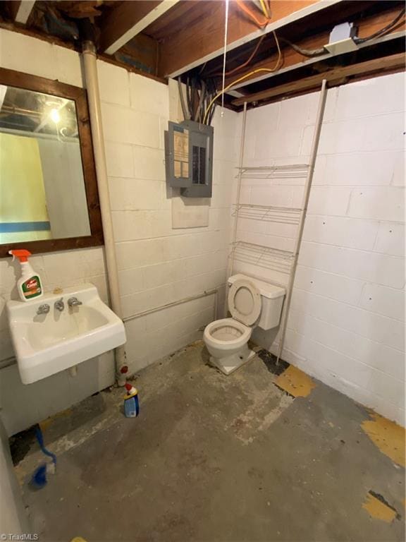 bathroom featuring toilet, concrete flooring, electric panel, and sink