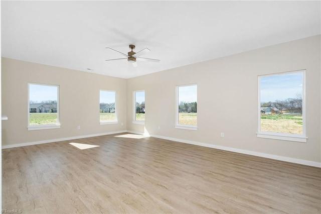 empty room featuring a wealth of natural light, ceiling fan, wood finished floors, and baseboards