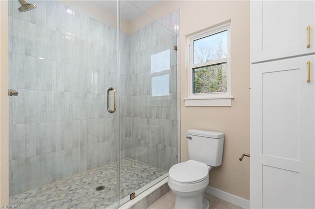 bathroom featuring toilet, a stall shower, baseboards, and tile patterned flooring