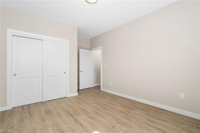 unfurnished bedroom featuring light wood-type flooring, a closet, and baseboards