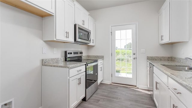 kitchen with stainless steel appliances, light stone counters, sink, light hardwood / wood-style flooring, and white cabinetry