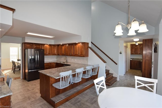 kitchen with an inviting chandelier, hanging light fixtures, decorative backsplash, black fridge with ice dispenser, and kitchen peninsula