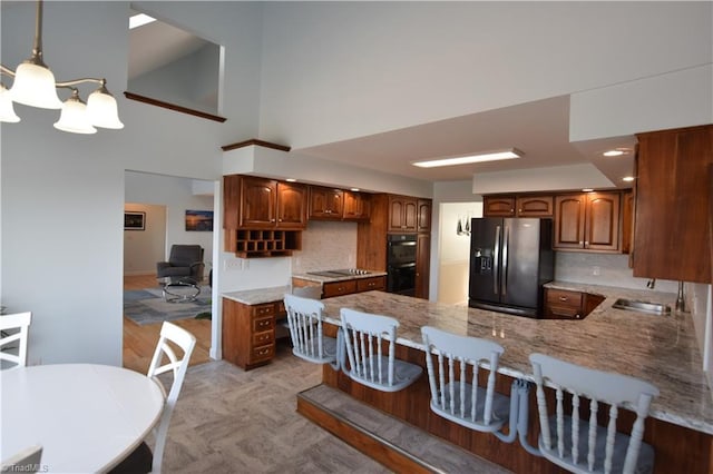 kitchen featuring black appliances, sink, decorative backsplash, hanging light fixtures, and kitchen peninsula