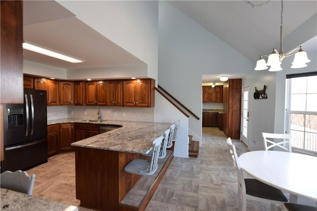 kitchen with sink, black fridge, decorative light fixtures, kitchen peninsula, and light stone countertops