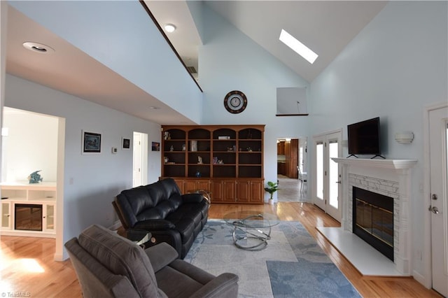 living room featuring built in shelves, a stone fireplace, vaulted ceiling with skylight, and light hardwood / wood-style flooring