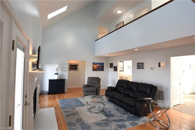 living room with a skylight, light hardwood / wood-style floors, and a high ceiling