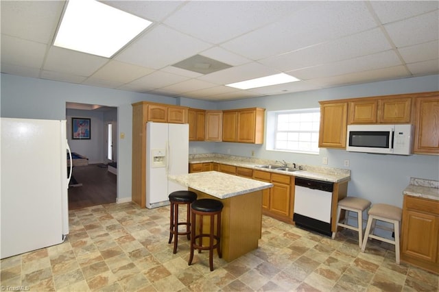 kitchen featuring sink, white appliances, a breakfast bar, a kitchen island, and a drop ceiling