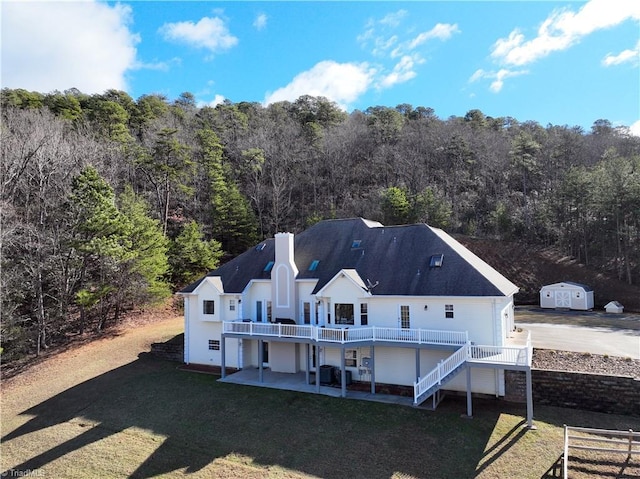 back of property featuring a storage shed, a deck, a patio area, and a lawn