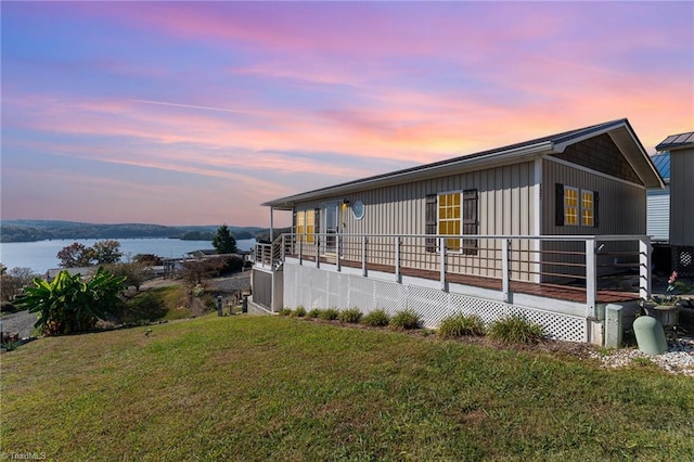 property exterior at dusk with a deck with water view and a yard