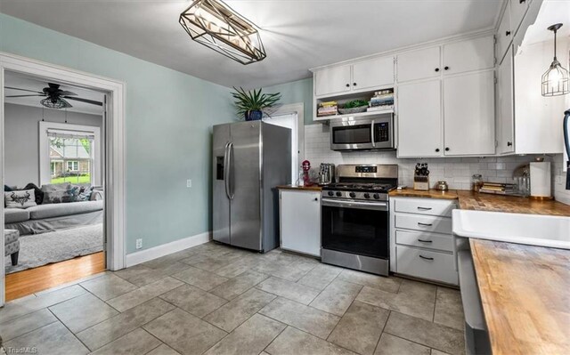 kitchen with stainless steel appliances, backsplash, wood counters, white cabinetry, and baseboards