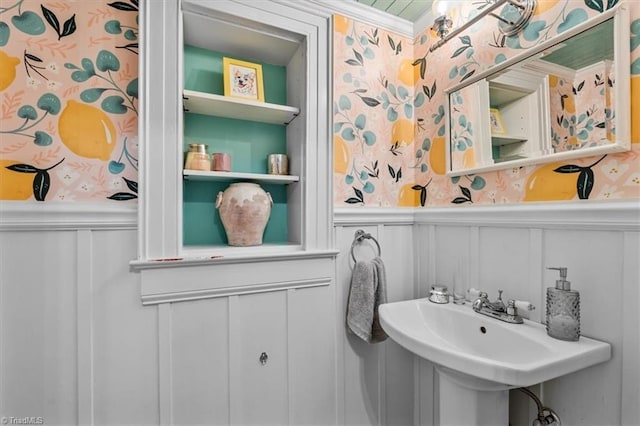 bathroom with a decorative wall, wallpapered walls, a wainscoted wall, ornamental molding, and a sink