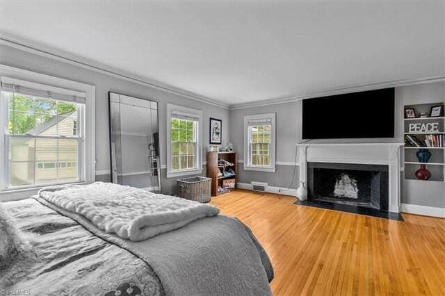 bedroom with crown molding, wood finished floors, a fireplace with flush hearth, and baseboards