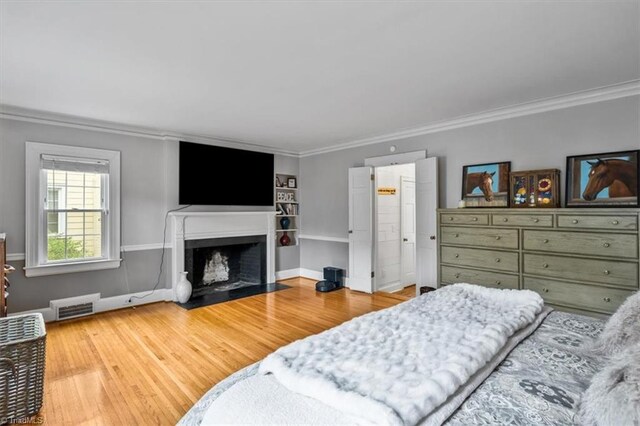 bedroom with ornamental molding, a fireplace with flush hearth, wood finished floors, and baseboards