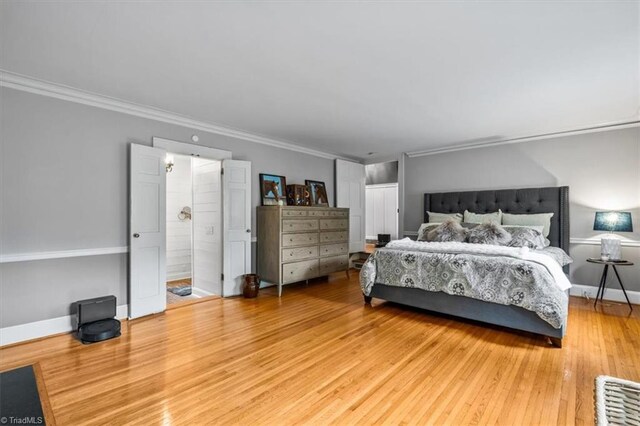 bedroom with wood finished floors, crown molding, baseboards, and ensuite bathroom