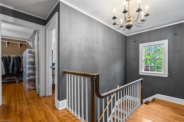 stairs with a chandelier, wood finished floors, ornamental molding, and baseboards