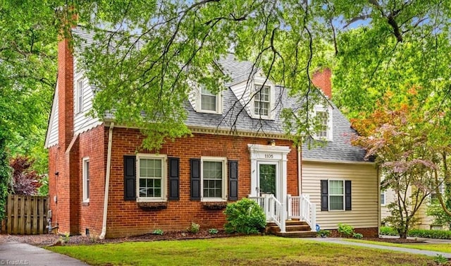 cape cod house with a chimney, brick siding, and a shingled roof