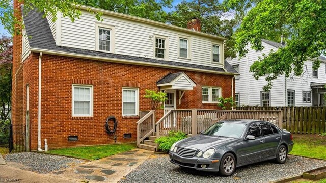 view of front of property featuring a chimney, brick siding, fence, and a shingled roof